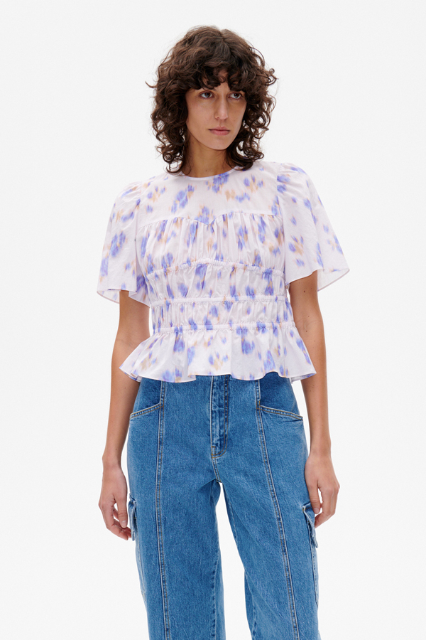 Marissa Top Purple Fleur Fanee This short sleeved top features elasticated panels throughout the body and a flare at the hem for a flattering silhouette - model image